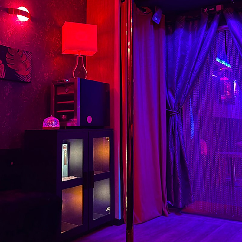 Intérieur de bar lounge avec pôle de danse brillant, éclairage néon rouge et violet. Meuble et lampe abat-jour rouge.
