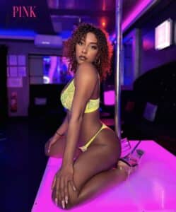 Femme en lingerie jaune fluo posant sur scène rose brillante, ambiance club néon. Texte 'PINK Palace' visible.